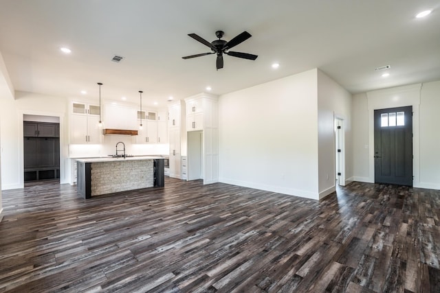 kitchen with pendant lighting, white cabinetry, sink, dark wood-type flooring, and a center island with sink