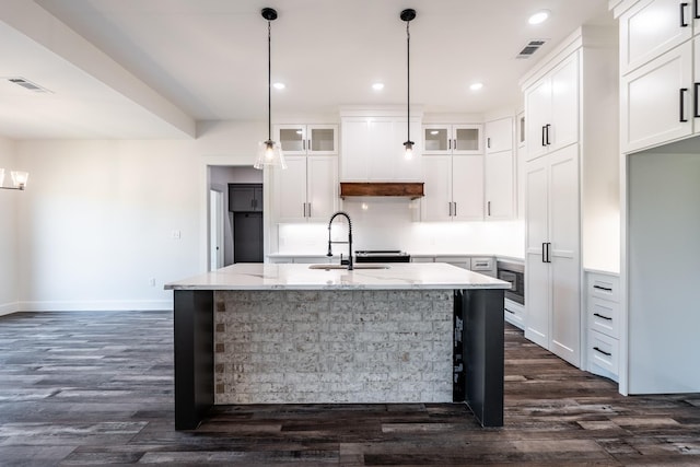 kitchen with white cabinetry, a kitchen island with sink, sink, and light stone counters