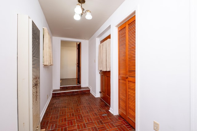 corridor with baseboards, a heating unit, brick patterned floor, and an inviting chandelier