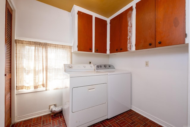 laundry room featuring baseboards, brick floor, cabinet space, and washing machine and clothes dryer