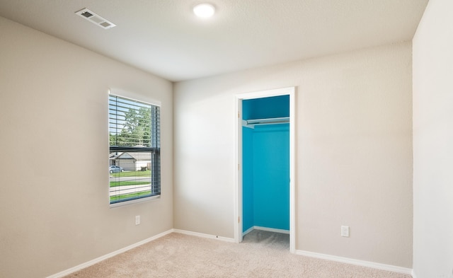 unfurnished bedroom featuring a closet, light colored carpet, and a spacious closet