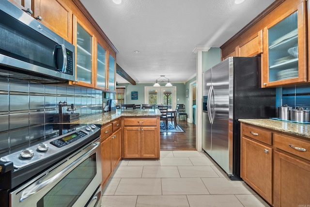 kitchen featuring glass insert cabinets, brown cabinets, light stone counters, a peninsula, and stainless steel appliances