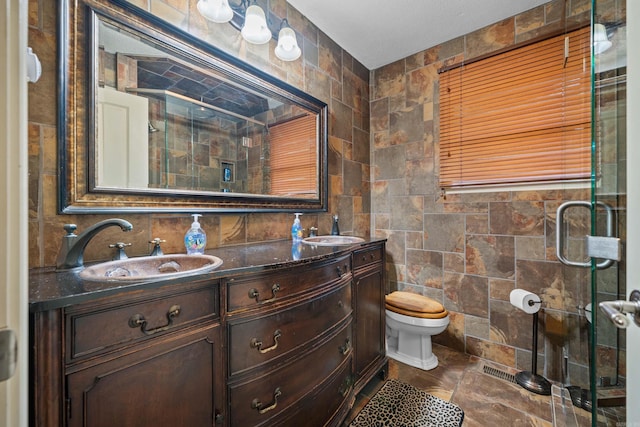 bathroom featuring double vanity, tile walls, toilet, a shower with shower door, and a sink