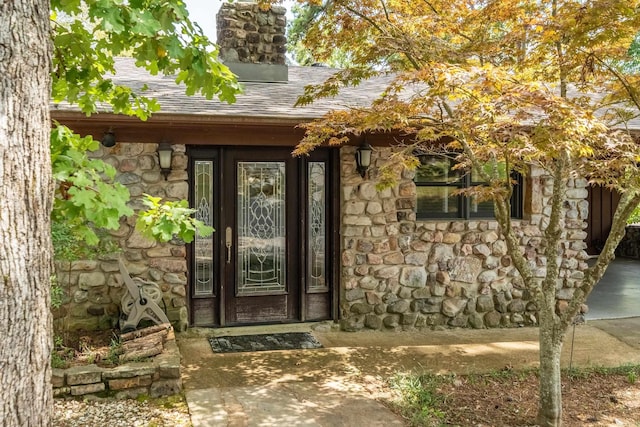 entrance to property featuring stone siding, a chimney, and roof with shingles