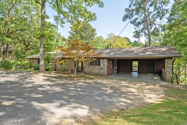 view of front of house with driveway, stone siding, and a carport