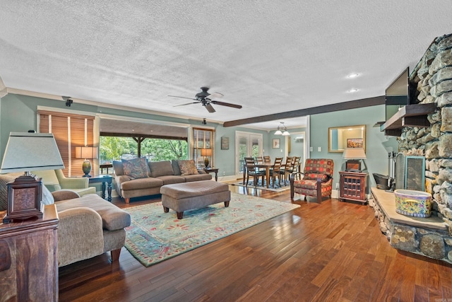 living area with a textured ceiling, a stone fireplace, wood finished floors, and a ceiling fan