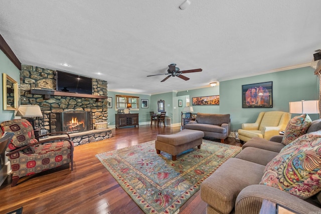 living room with a textured ceiling, a stone fireplace, wood finished floors, baseboards, and ornamental molding