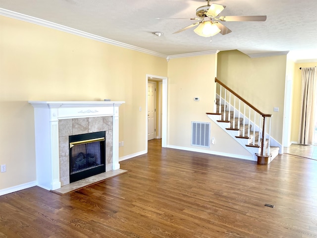 unfurnished living room with crown molding, dark wood-type flooring, a tile fireplace, ceiling fan, and a textured ceiling