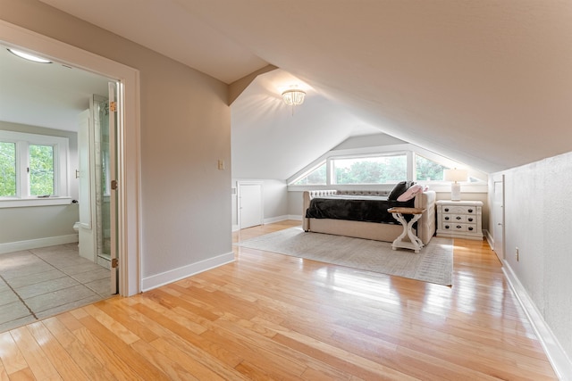 unfurnished bedroom with ensuite bath, light hardwood / wood-style flooring, and lofted ceiling