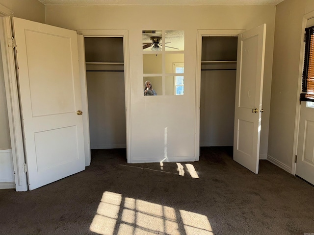 unfurnished bedroom featuring dark colored carpet and two closets