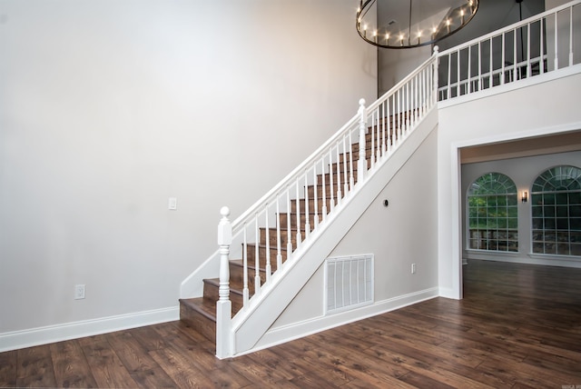 staircase featuring dark hardwood / wood-style flooring, an inviting chandelier, and a high ceiling