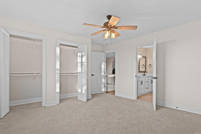 unfurnished bedroom featuring ensuite bathroom, sink, multiple closets, light carpet, and ceiling fan