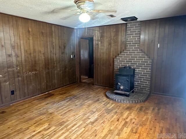 unfurnished living room featuring visible vents, wood finished floors, a wood stove, and a ceiling fan