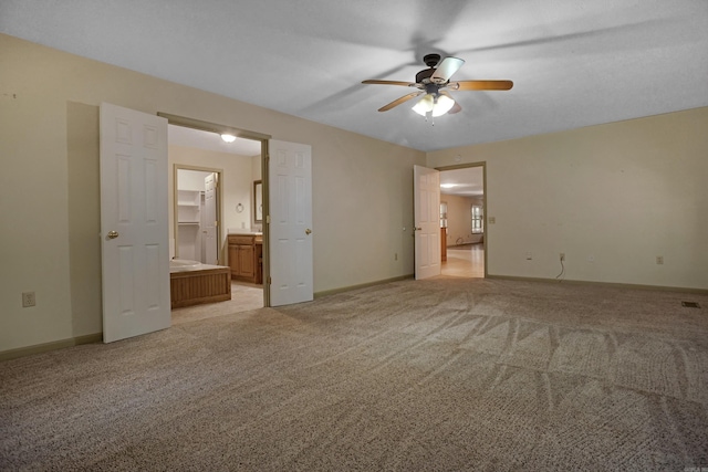 unfurnished bedroom featuring light carpet, a walk in closet, ensuite bath, and ceiling fan