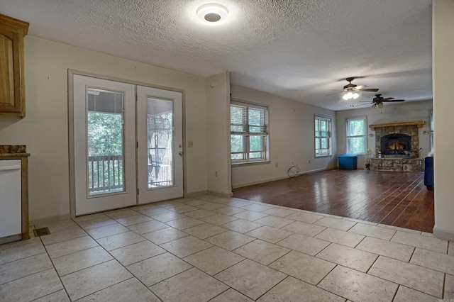 interior space with a stone fireplace, a textured ceiling, ceiling fan, and light wood-type flooring