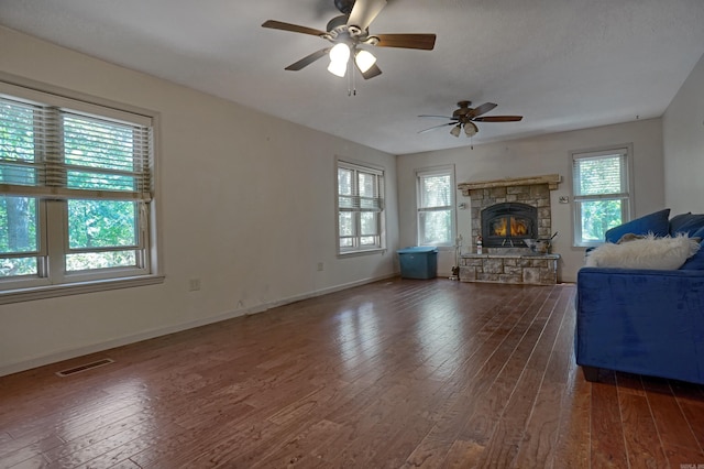 unfurnished living room featuring ceiling fan, dark hardwood / wood-style flooring, and a stone fireplace