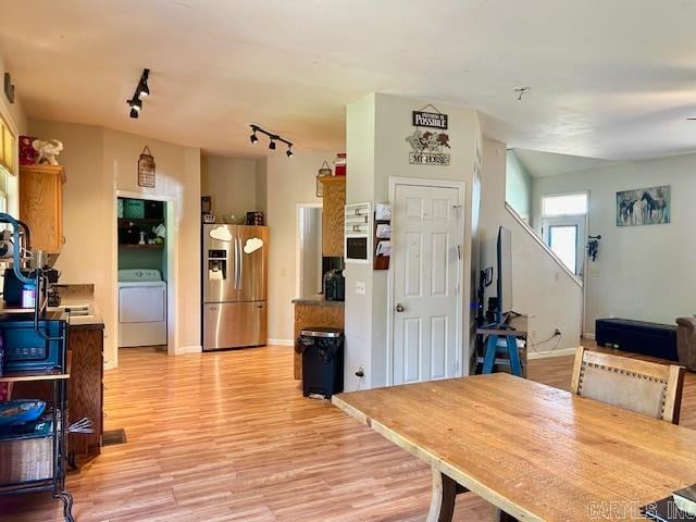 interior space featuring washer / dryer, track lighting, light hardwood / wood-style flooring, and stainless steel refrigerator with ice dispenser