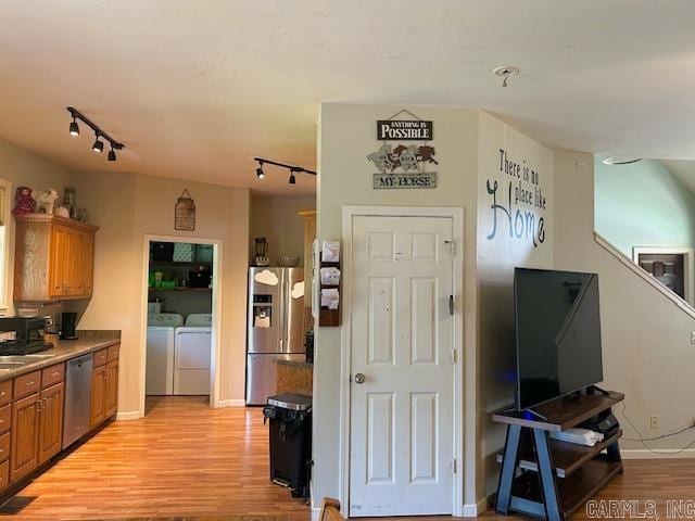 kitchen featuring light hardwood / wood-style floors, track lighting, washing machine and dryer, and stainless steel appliances