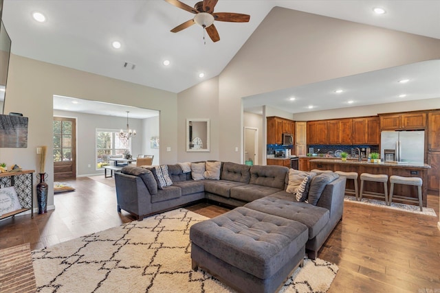 living room featuring high vaulted ceiling, ceiling fan with notable chandelier, and light wood-type flooring