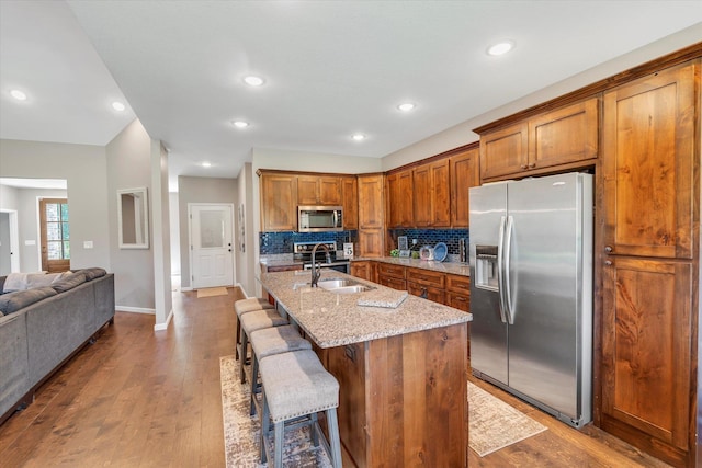 kitchen featuring a kitchen island with sink, stainless steel appliances, light stone counters, tasteful backsplash, and a kitchen bar