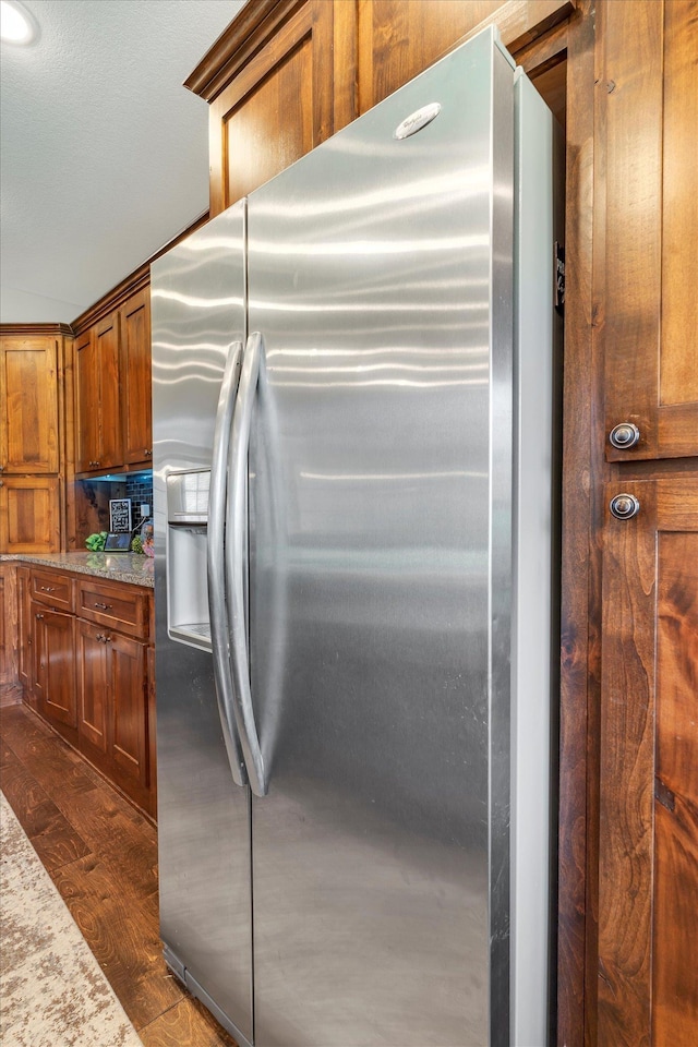 kitchen with dark hardwood / wood-style flooring, stainless steel fridge, and light stone countertops