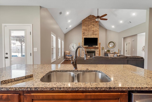 kitchen featuring lofted ceiling, sink, light stone counters, ceiling fan, and a fireplace