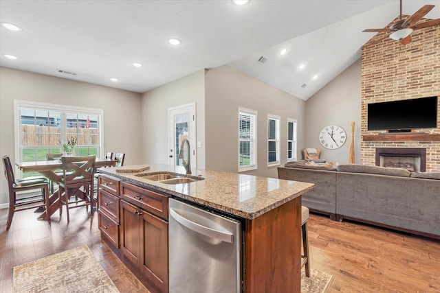 kitchen with hardwood / wood-style floors, an island with sink, sink, stainless steel dishwasher, and a brick fireplace