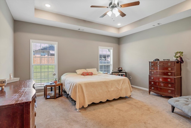 bedroom featuring multiple windows, light carpet, ceiling fan, and a tray ceiling