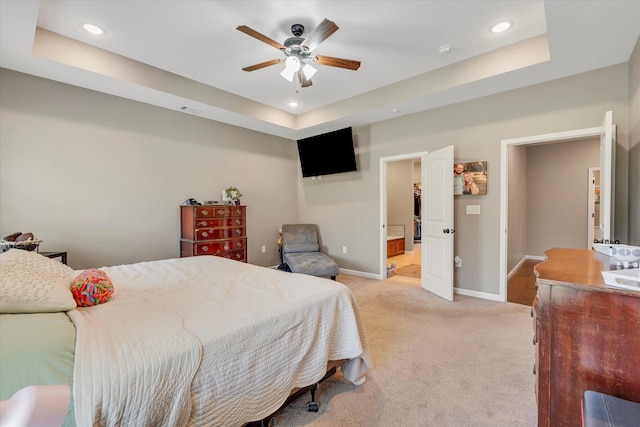 bedroom with ceiling fan, light colored carpet, and a tray ceiling