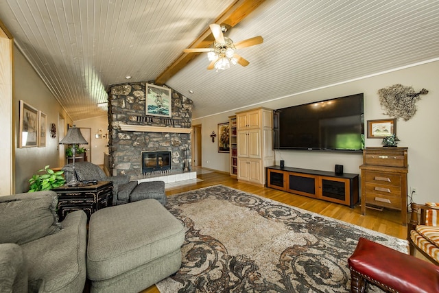 living room with ceiling fan, a stone fireplace, light hardwood / wood-style floors, and vaulted ceiling with beams