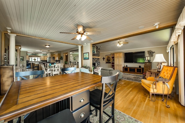 dining room with ceiling fan, a fireplace, decorative columns, and light wood-type flooring