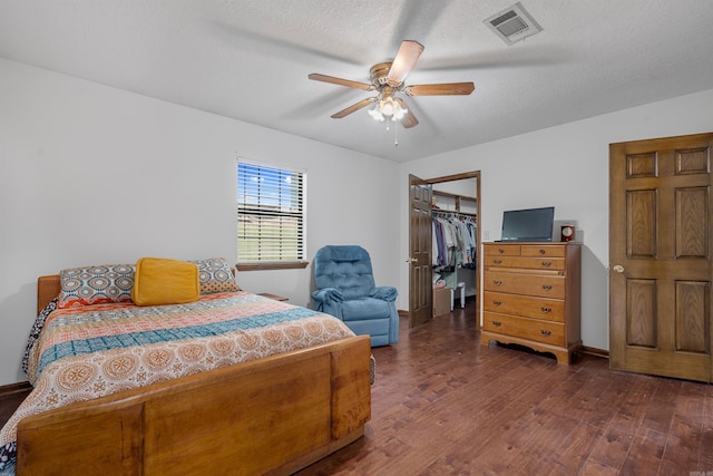 bedroom with a textured ceiling, dark hardwood / wood-style flooring, a spacious closet, ceiling fan, and a closet