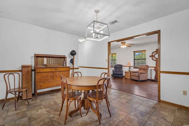 dining area with a textured ceiling, ceiling fan with notable chandelier, and dark tile patterned flooring