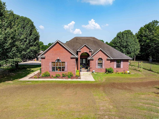 view of front of home featuring roof with shingles, fence, a front lawn, and brick siding