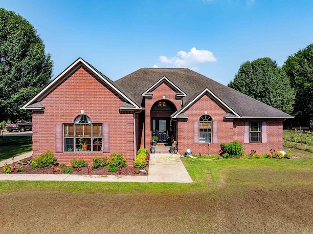 traditional home with a shingled roof, brick siding, a patio, and a front lawn