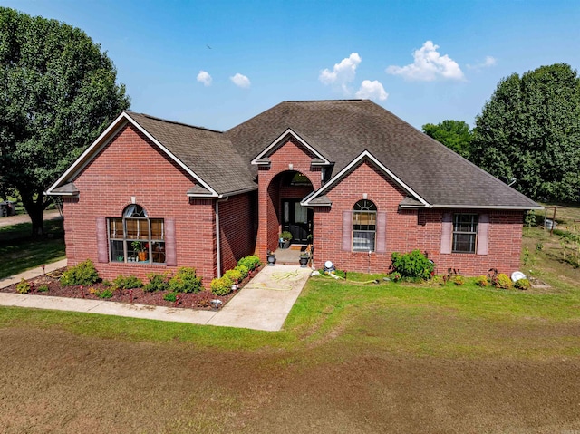 view of front of property with a shingled roof, brick siding, and a front lawn