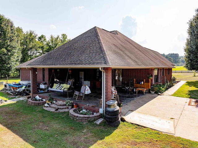 exterior space with a patio area, brick siding, a yard, and roof with shingles