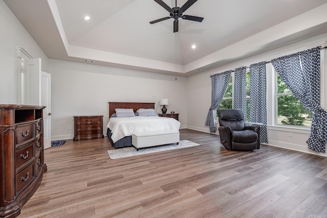 bedroom featuring high vaulted ceiling, light hardwood / wood-style flooring, ceiling fan, and a raised ceiling