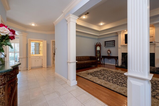 entrance foyer with decorative columns, a fireplace, crown molding, and light wood-type flooring