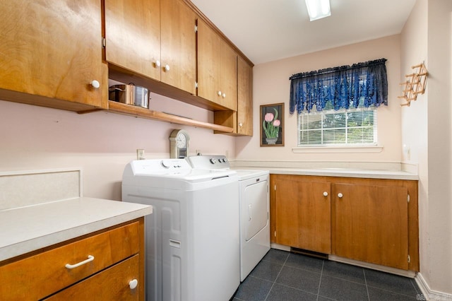 clothes washing area with dark tile patterned floors, washing machine and clothes dryer, and cabinets