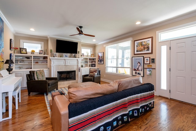 living room featuring ceiling fan, a tiled fireplace, hardwood / wood-style flooring, and crown molding