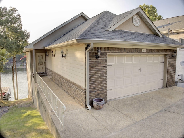 view of property exterior featuring a shingled roof, brick siding, a water view, and a garage