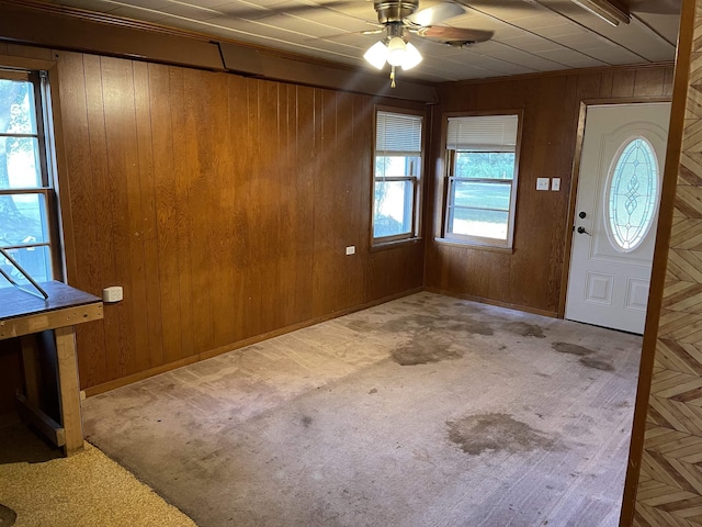 foyer entrance featuring a healthy amount of sunlight, wooden walls, and light carpet