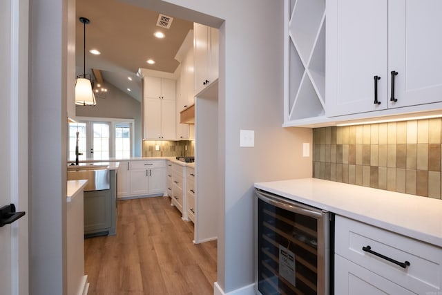 kitchen with vaulted ceiling, light hardwood / wood-style flooring, pendant lighting, beverage cooler, and white cabinets