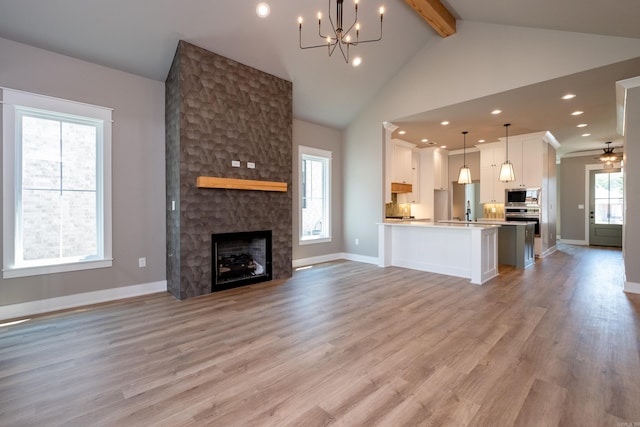 unfurnished living room featuring sink, beam ceiling, light hardwood / wood-style floors, a stone fireplace, and a chandelier