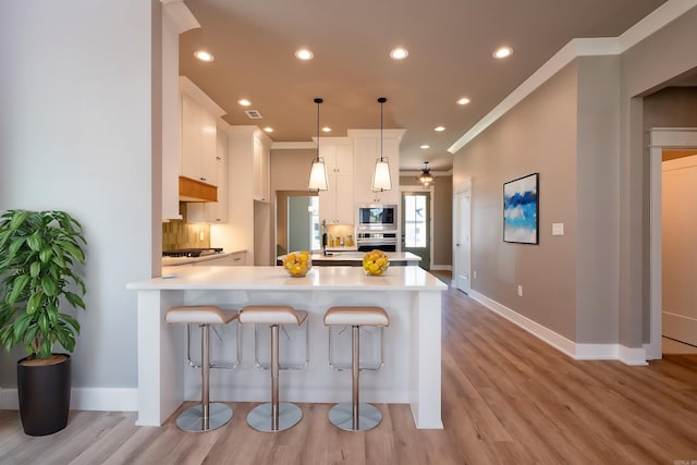 kitchen featuring white cabinetry, light wood-type flooring, ornamental molding, appliances with stainless steel finishes, and pendant lighting