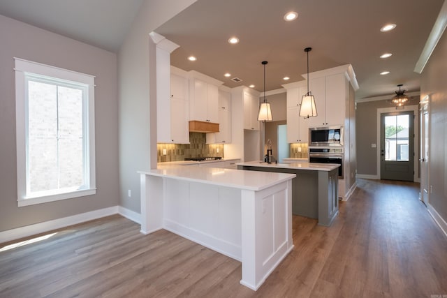 kitchen featuring appliances with stainless steel finishes, pendant lighting, white cabinets, decorative backsplash, and kitchen peninsula