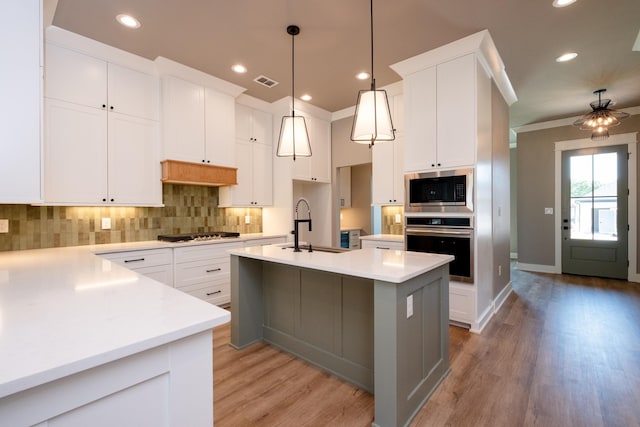 kitchen featuring sink, decorative light fixtures, a center island with sink, stainless steel appliances, and white cabinets