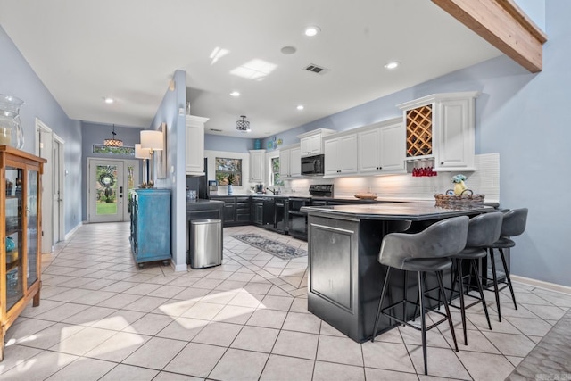 kitchen with beam ceiling, black appliances, light tile patterned floors, and white cabinetry