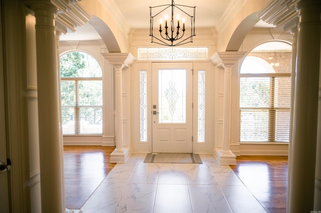 foyer entrance featuring decorative columns, wood-type flooring, crown molding, and a chandelier